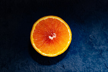 Top view of round orange slice. Ripe orange fruit on dark blue background. Dark low key photo. Copy space. Blurred background. Copy space.
