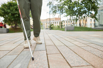 Low angle shot of blind man walking in city and using cane on pavement, copy space © Seventyfour