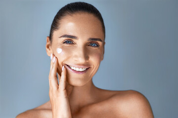 Anti-aging cosmetics. Portrait of beautiful mature woman applaing face skin care product ,smiling,...