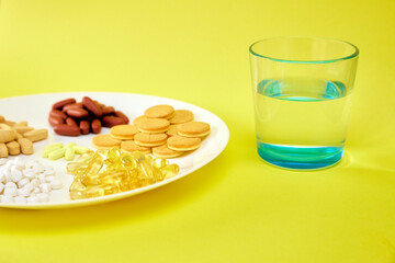A handful of pills, capsules and multi-colored tablets on a plate next to cutlery. Taking medication. Pills instead of food. The concept of vitamins instead of food