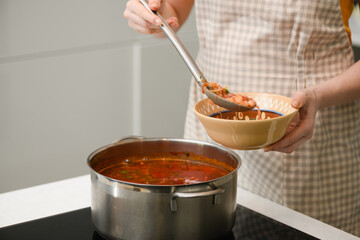 A woman pours freshly prepared Ukrainian borscht onto a plate.