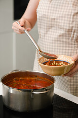 A woman pours freshly prepared Ukrainian borscht onto a plate.