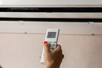 A woman's hand holds a remote control to turn on the air conditioner