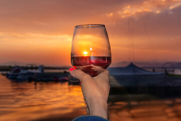 a girl holds in her hand rose wine or champagne in a glass on the seashore in the evening at sunset