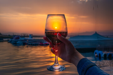 a girl holds in her hand rose wine or champagne in a glass on the seashore in the evening at sunset