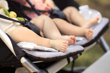 Fototapeta na wymiar Closeup two little twin baby girls 6 month old walking in a double stroller in city park