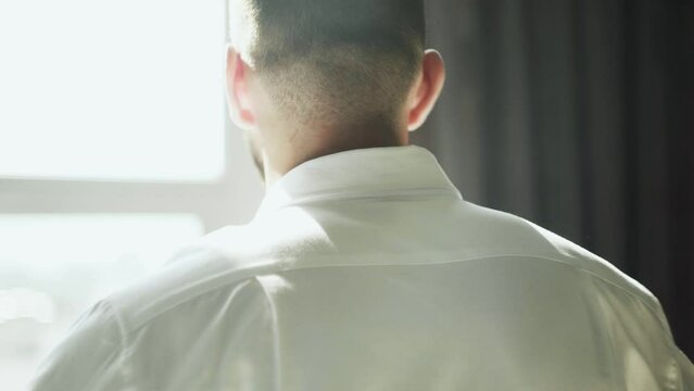Back view of handsome man puts oa white shirt