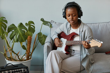 Minimal portrait of black young woman playing electronic guitar at home and singing, copy space