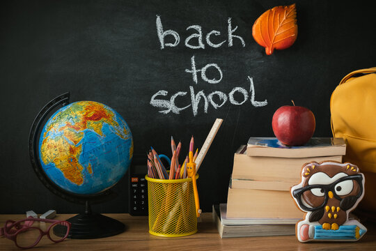 School supplies next to the globe and stack of books on the blackboard background. Back to school concept on September day