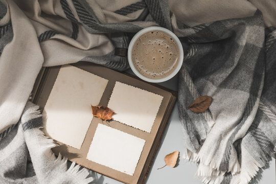 Clear blank photo frames on old album, cup of coffee with grey plaid and fall leaves. Sunday loneliness relaxing, hugge mood. Family traditions, memories and nostalgia concept. Flat lay. Autumn vibes.