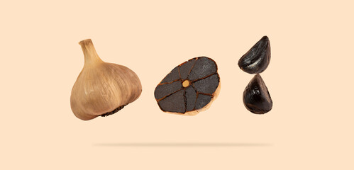 Black garlic bulbs float in the air on a beige background. An image of flying black garlic. Concept...