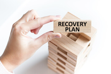 RECOVERY PLAN text on a wooden bar in the hand of a girl next to the tower of the game jenga