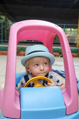 Fototapeta na wymiar happy blond cute child in the hat on the playground in the colorful toy car