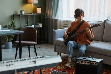 Full length portrait of young man playing electric guitar in cozy home music studio, copy space