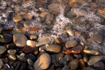 A pure transparent sea wave rolls over the rocky pebble shore, the concept of rest and travel, tranquility, relaxation and reflection on a warm summer day, close-up.