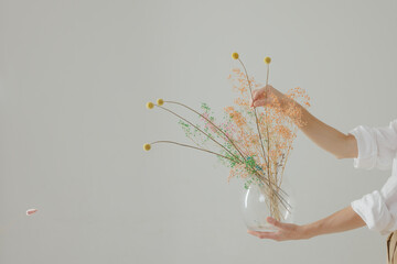 female hands hold a transparent glass vase with dried flowers on a light background