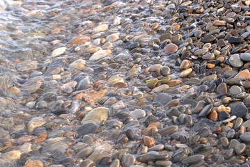 A pure transparent sea wave rolls over the rocky pebble shore, the concept of rest and travel, tranquility, relaxation and reflection on a warm summer day, close-up.