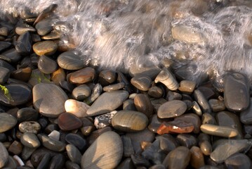 A pure transparent sea wave rolls over the rocky pebble shore, the concept of rest and travel, tranquility, relaxation and reflection on a warm summer day, close-up.
