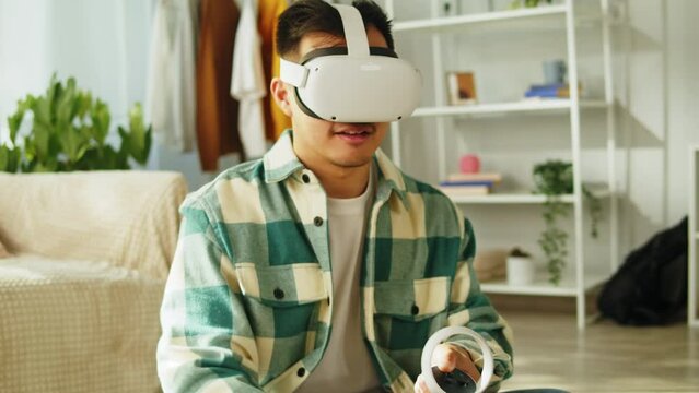 Korean man using virtual reality glasses with controllers, playing video games, Asian guy gamer wearing new generation gaming headset for entertainment at home, future technology concept.