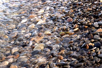 A pure transparent sea wave rolls over the rocky pebble shore, the concept of rest and travel, tranquility, relaxation and reflection on a warm summer day, close-up.
