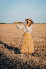 Rural woman plays on wooden flute - ukrainian telenka, tylynka in wheat field. Folk music, sopilka concept. Musical instrument. Musician in traditional embroidered shirt - Vyshyvanka.
