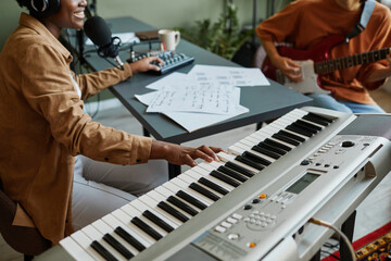 Closeup of black young woman pressing piano keys while composing music with band of young musicians