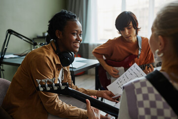 Side view portrait of black young woman writing music with band and smiling happily