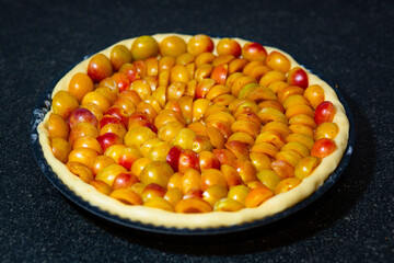Raw Mirabelle plum tart not yet baked in backing pan on a black stone surface