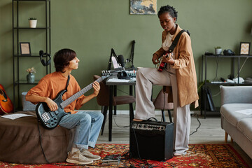 Full length shot of two young musicians playing guitars together while composing songs in cozy...