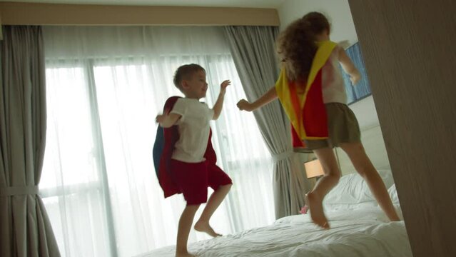 Children playing superheroes, are jumping in room on bed,in children's room, two children in red and blue Superman costume, Superheroes, brother and sister, play at home imagining they are superheroes