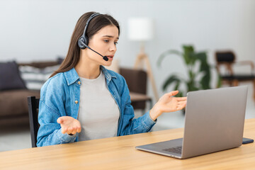 Concentrated woman support worker in headphones is working at modern office. Portrait of female call center employee consults client online using video call, reporting bad news - obrazy, fototapety, plakaty