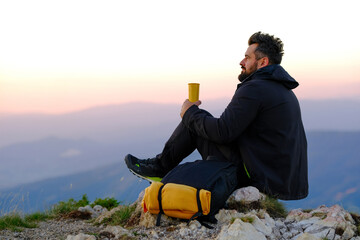 A happy traveler man is relaxing while drinking a cup of coffee during the hike on the mountain.	