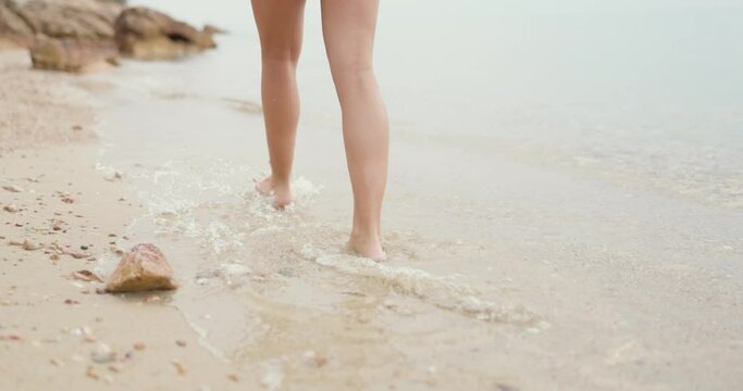 Close-up of an unrecognizable female teenager's legs is walking along the empty sandy sea beach.