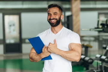 Tuinposter Portrait of personal trainer holding clipboard with training plan in gym © Igor