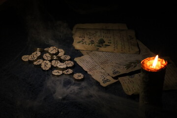 On Halloween night, in the light of a burning candle, runes and old sheets of a book are wrapped in...