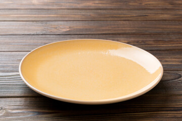 Perspective view of empty orange plate on wooden background. Empty space for your design