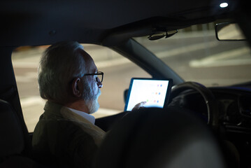 Senior man sitting in the car and using navigation system on parking lot at night 