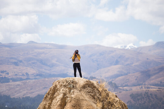 Mujer turista tomando fotos con una cámara profesional desde lo alto de una montaña con montañas alrededor. Concepto de personas, estilos de vida, turismo y aventura.