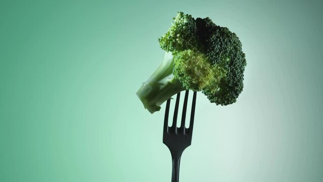 Broccoli impaled on a fork rotates on a green background.