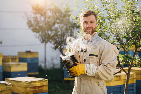 Portrait of the male beekeeper smoking the honeycomb of a beehive with bees swarming around them