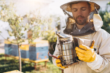 Portrait of a happy male beekeeper working in an apiary near beehives with bees. Collect honey. Beekeeper on apiary. Beekeeping concept. - obrazy, fototapety, plakaty
