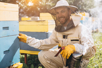 Portrait of a happy male beekeeper working in an apiary near beehives with bees. Collect honey....