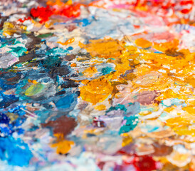 The artist's palette with multicolored smeared paints. A street artist's palette of smeared colors in bright sunlight close-up. Oil paints and gouache on a wooden palette.