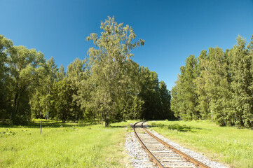 a single-track old railway in a green forest against a blue sky