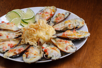 Baked mussels au gratin with mashed potatoes on a white plate on wooden table. Brazilian seafood.