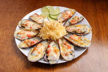 Baked mussels au gratin with mashed potatoes on a white plate on wooden table. Brazilian seafood.