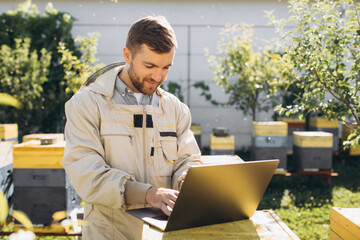 Male agronomist or engineer in protective suit working on laptop at bee farm