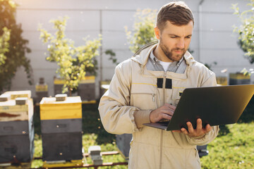 Male agronomist or engineer in protective suit working on laptop at bee farm