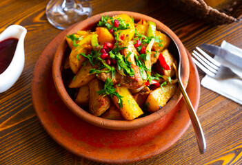 Appetizing spicy Ojakhuri from roasted pork with potatoes and onions garnished with fresh greens served with pomegranate sauce in traditional clay ketsi pan. Authentic Georgian cuisine