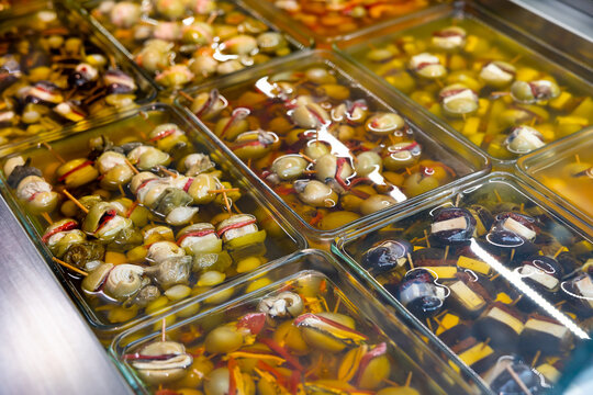 Large assortment of pickled olives stuffed with cheese, seafood and vegetables displayed in glass containers on market counter. Traditional spanish appetizer